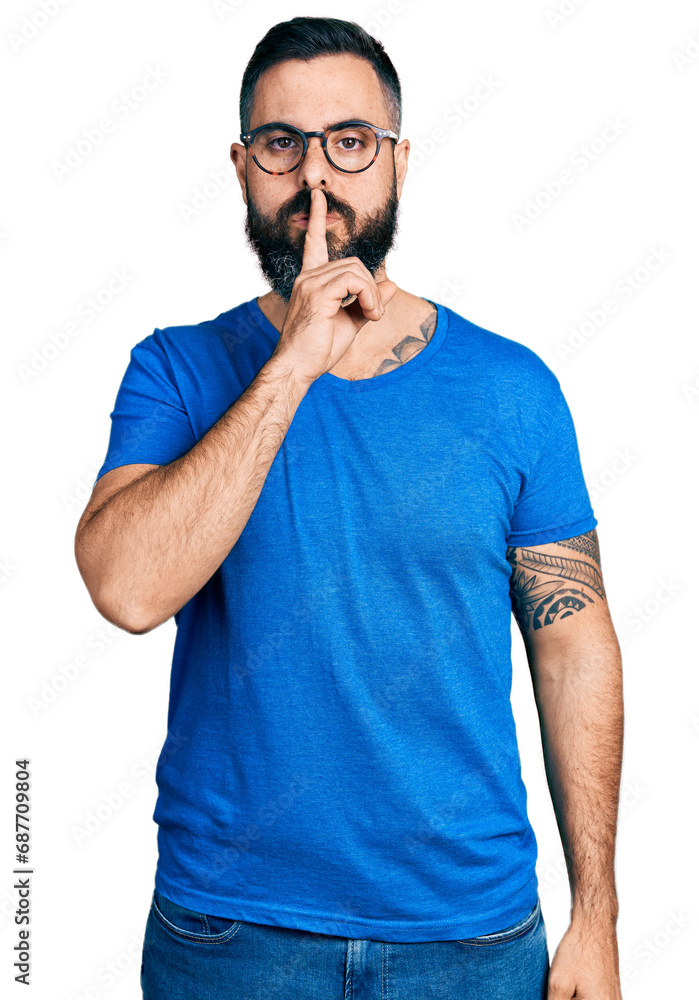 Hispanic man with beard wearing casual t shirt and glasses asking to be quiet with finger on lips. silence and secret concept. Hispanic man with beard wearing casual t shirt and glasses asking to be quiet with finger on lips. silence and secret concept.