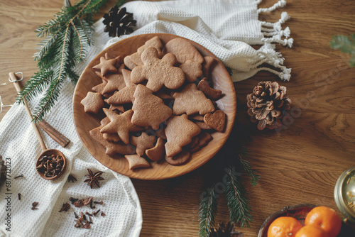 Christmas gingerbread cookies in wooden plate on rustic table flat lay with fir branches, pinecone, spices. Merry Christmas! Delicious fresh gingerbread cookies close up, atmospheric holiday