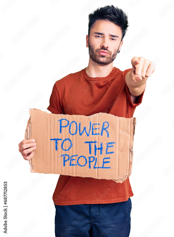 Young hispanic man holding power to the people banner pointing with finger to the camera and to you, confident gesture looking serious Young hispanic man holding power to the people banner pointing with finger to the camera and to you, confident gesture looking serious