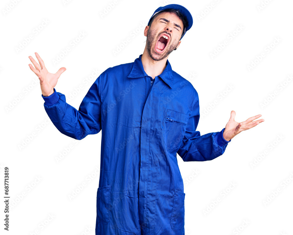 Young hispanic man wearing painter uniform crazy and mad shouting and yelling with aggressive expression and arms raised. frustration concept.