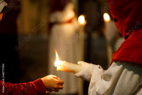 A Nazarene giving a candle to a child during Holy Week   photo