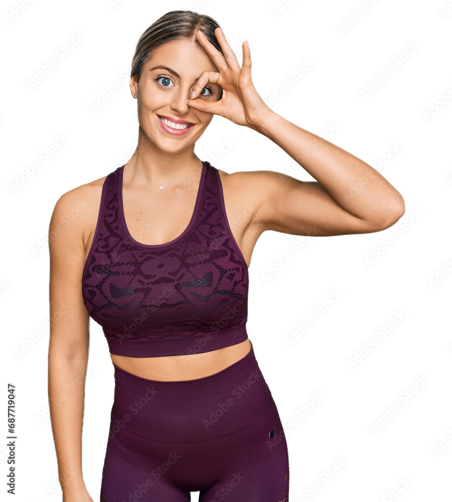 Beautiful blonde woman wearing sportswear smiling happy doing ok sign with hand on eye looking through fingers Beautiful blonde woman wearing sportswear smiling happy doing ok sign with hand on eye looking through fingers