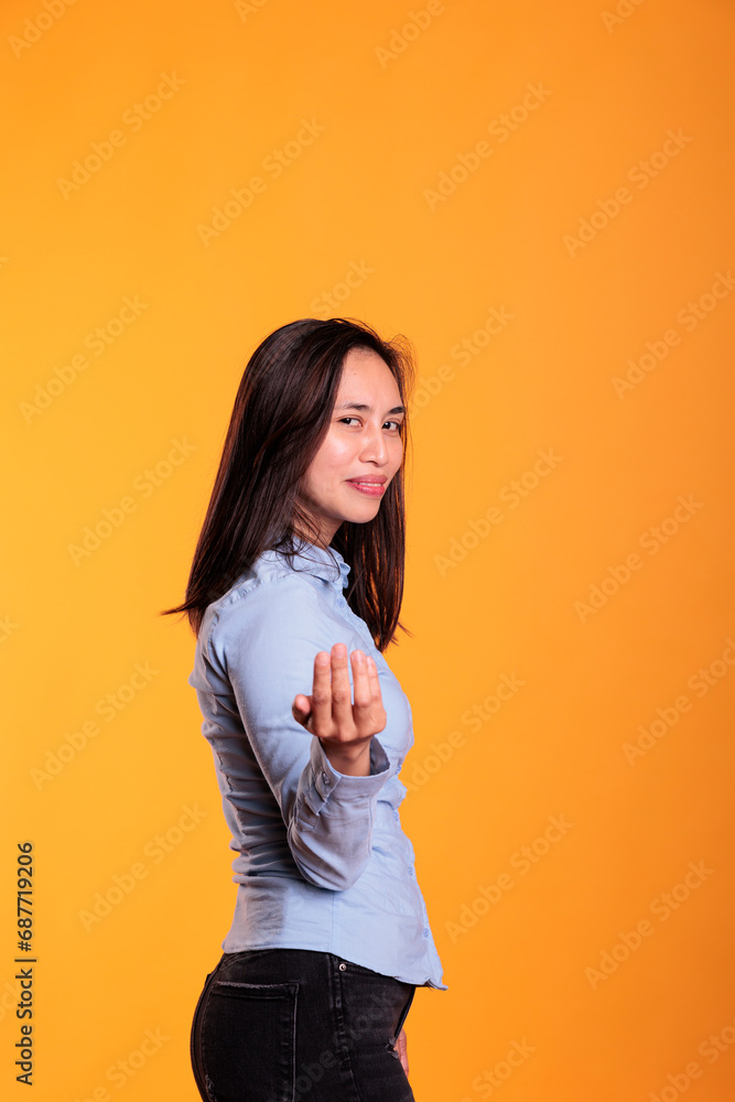 Attractive asian woman inviting you to come here with a friendly smile on her confident expression, posing in studio over yellow background. Joyful young adult is calling out with a finger gesture Attractive asian woman inviting you to come here with a friendly smile on her confident expression, posing in studio over yellow background. Joyful young adult is calling out with a finger gesture