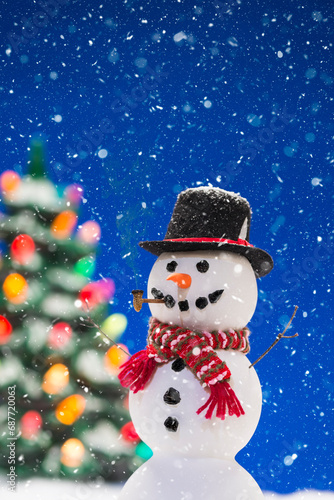 A happy snowman wearing a top hat with Christmas tree in background while snowing © CMANNPHOTO