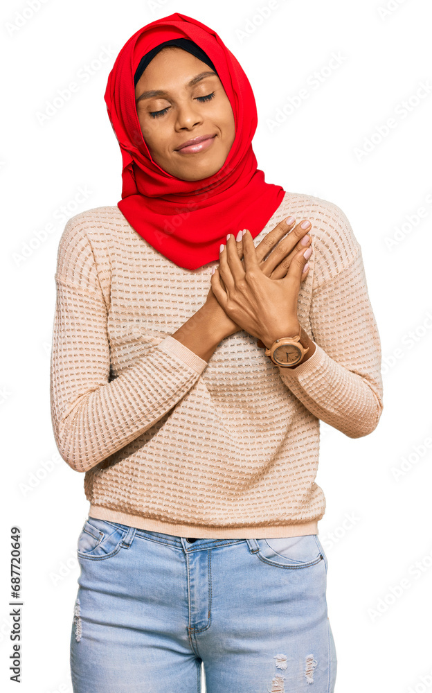 Young african american woman wearing traditional islamic hijab scarf smiling with hands on chest with closed eyes and grateful gesture on face. health concept. Young african american woman wearing traditional islamic hijab scarf smiling with hands on chest with closed eyes and grateful gesture on face. health concept.