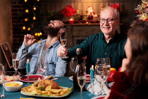Old adult giving toast with raised glass of champagne at christmas eve celebration to enjoy winter holiday with friends and family. Grandpa making speech around the table  sparkling wine.