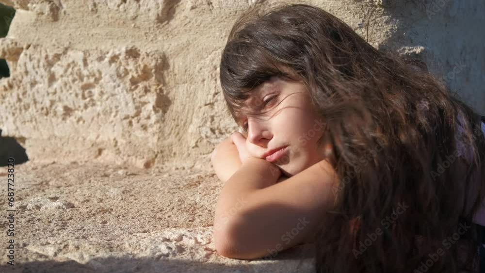 Thoughtful girl by fortress wall. A nice thoughtful child sitting by the fortress old wall and think about something in the sun light. Thoughtful girl by fortress wall. A nice thoughtful child sitting by the fortress old wall and think about something in the sun light.