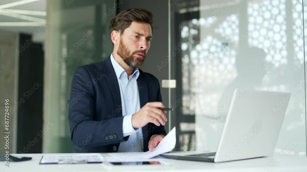 Busy financier in formal suit making financial calculations using calculator, typing on a laptop taking notes sitting at workplace. Confident businessman working fills out documents in business office Busy financier in formal suit making financial calculations using calculator, typing on a laptop taking notes sitting at workplace. Confident businessman working fills out documents in business office