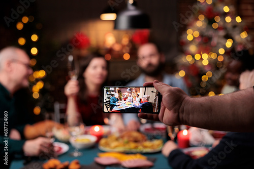 Man taking photo of family at dinner, celebrating christmas eve holiday with traditional food and drink. Someone takes pictures of people enjoying feast with glasses of wine during celebration.