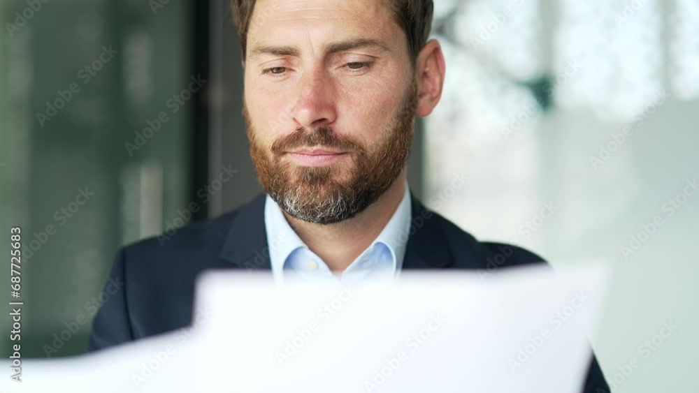 Serious thoughtful businessman holds documents in his hands, looks at the report sitting at a workplace in business office. Financier is satisfied with the results of a financial statement. Close up Serious thoughtful businessman holds documents in his hands, looks at the report sitting at a workplace in business office. Financier is satisfied with the results of a financial statement. Close up