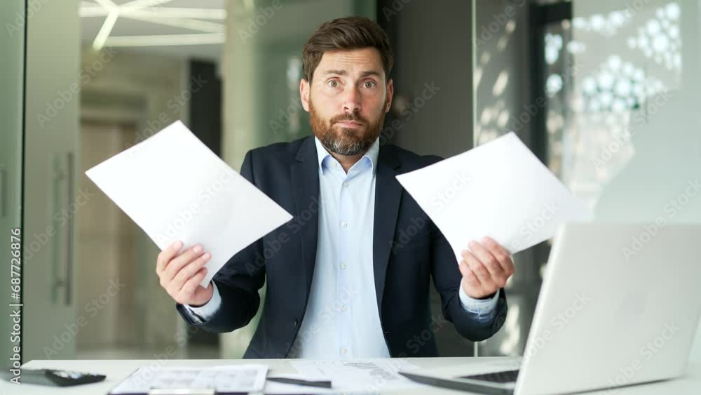Confused businessman in a formal suit having difficulty with paper work sitting at desk at workplace in business office. Puzzled entrepreneur looks at the documents and cannot understand the problem Confused businessman in a formal suit having difficulty with paper work sitting at desk at workplace in business office. Puzzled entrepreneur looks at the documents and cannot understand the problem