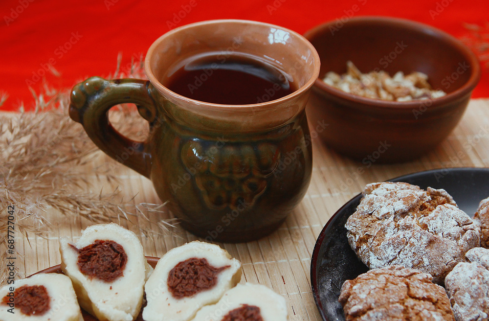 Fototapeta premium Homemade baked goods - handmade grilled cookies, chopped dumplings, nuts, clay cup of tea on a red background.