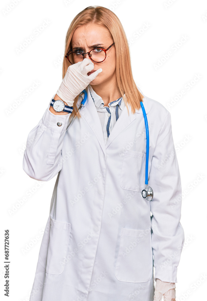 Beautiful caucasian woman wearing doctor uniform and stethoscope smelling something stinky and disgusting, intolerable smell, holding breath with fingers on nose. bad smell Beautiful caucasian woman wearing doctor uniform and stethoscope smelling something stinky and disgusting, intolerable smell, holding breath with fingers on nose. bad smell