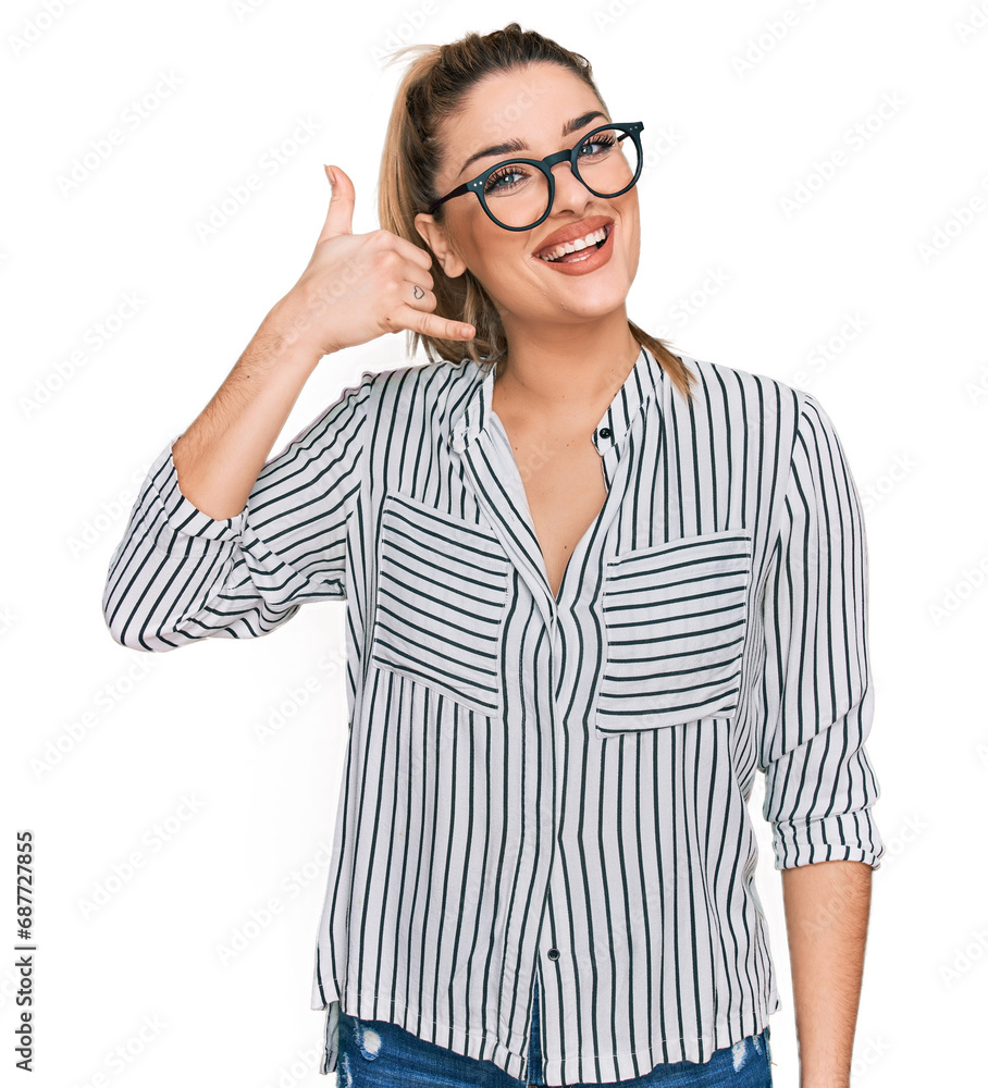 Young caucasian woman wearing business shirt and glasses smiling doing phone gesture with hand and fingers like talking on the telephone. communicating concepts. Young caucasian woman wearing business shirt and glasses smiling doing phone gesture with hand and fingers like talking on the telephone. communicating concepts.
