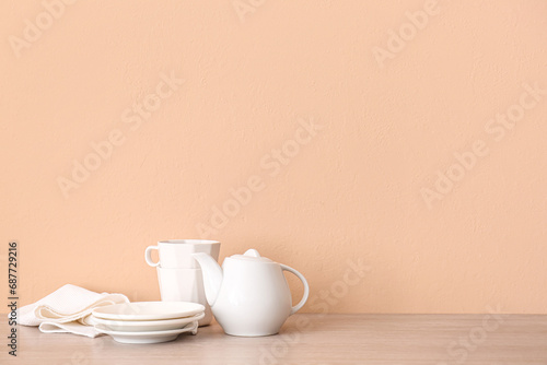 Set of white crockery on wooden table near beige wall