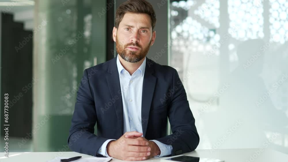 Webcam view. Businessman in a formal suit watching video call training looking at camera while sitting at workplace in office. Male is studying online, listening remotely to a course, webinar, seminar Webcam view. Businessman in a formal suit watching video call training looking at camera while sitting at workplace in office. Male is studying online, listening remotely to a course, webinar, seminar