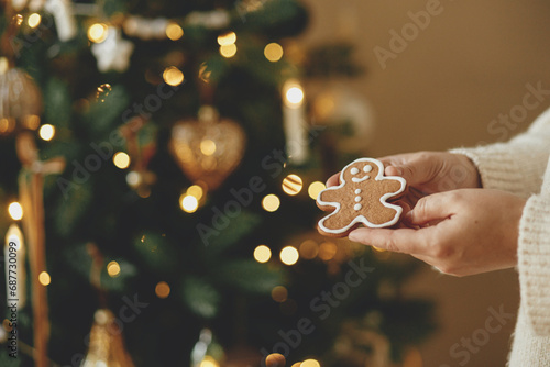 Hand holding christmas gingerbrea man cookie with icing against festive christmas tree with golden lights bokeh. Merry Christmas! Delicious gingerbread cookies, atmospheric holiday time photo