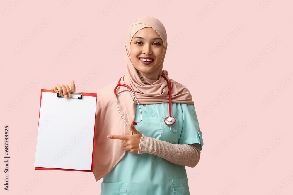Female Muslim doctor in hijab with clipboard on pink background. World Hijab Day concept Female Muslim doctor in hijab with clipboard on pink background. World Hijab Day concept