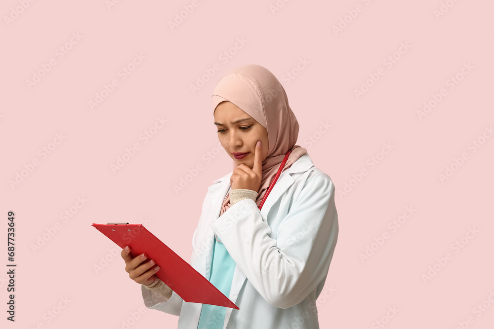 Female Muslim doctor in hijab with clipboard on pink background. World Hijab Day concept Female Muslim doctor in hijab with clipboard on pink background. World Hijab Day concept