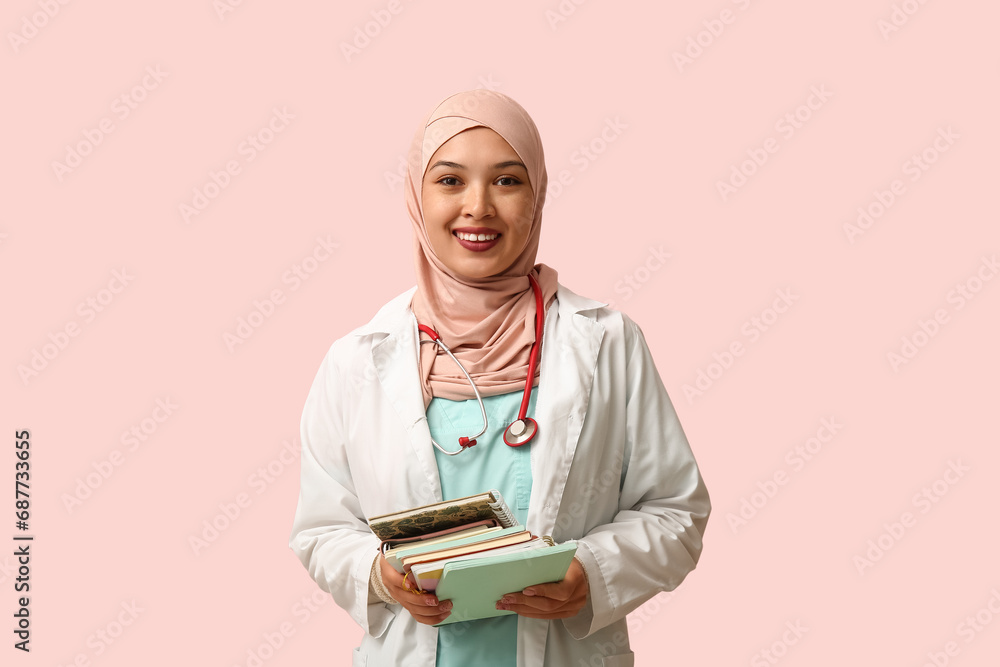 Fototapeta premium Female Muslim doctor in hijab with journals on pink background. World Hijab Day concept