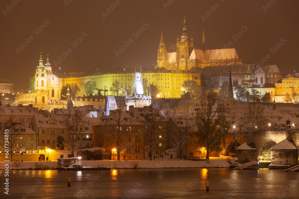The night snowy Prague Lesser Town with gothic Castle and Charles Bridge above River Vltava, Czech Republic