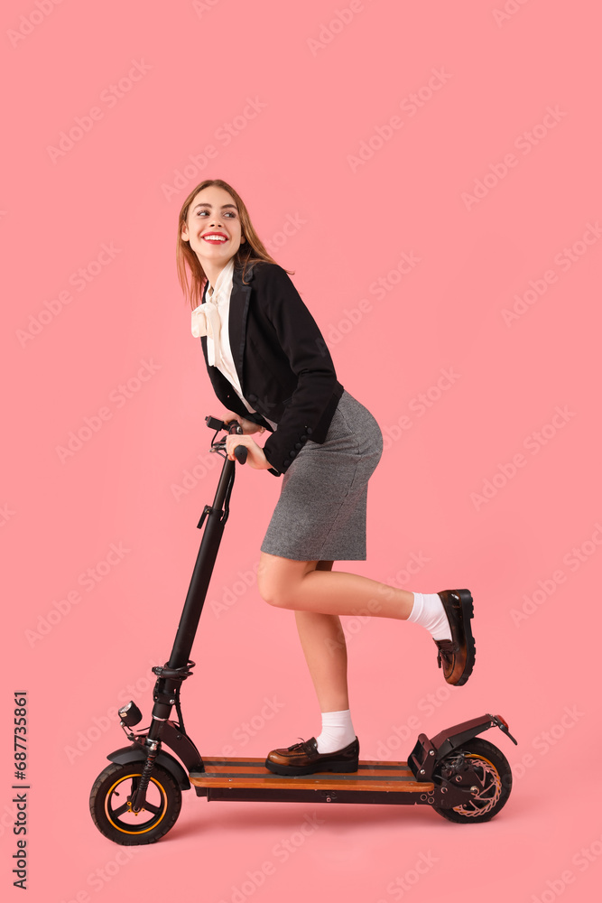 Portrait of young businesswoman riding kick scooter on pink background Portrait of young businesswoman riding kick scooter on pink background