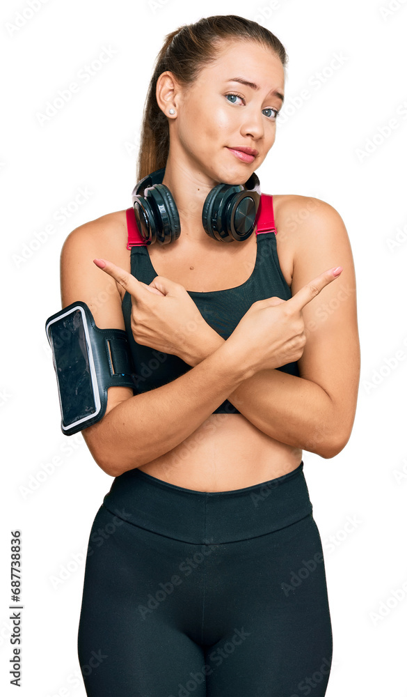Beautiful blonde woman wearing gym clothes and using headphones pointing to both sides with fingers, different direction disagree Beautiful blonde woman wearing gym clothes and using headphones pointing to both sides with fingers, different direction disagree