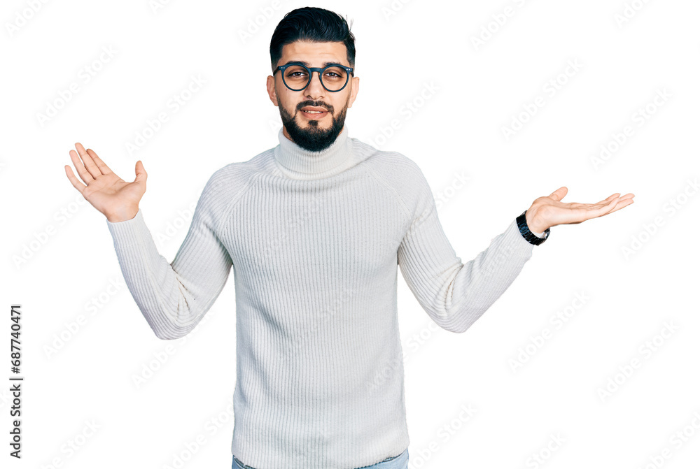 Young arab man with beard wearing elegant turtleneck sweater and glasses clueless and confused expression with arms and hands raised. doubt concept.
