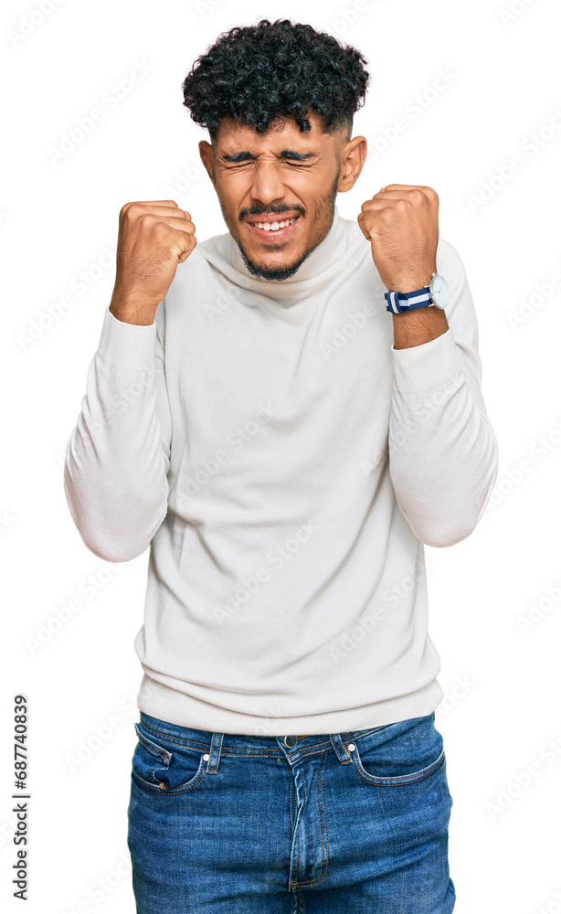Young arab man wearing casual winter sweater excited for success with arms raised and eyes closed celebrating victory smiling. winner concept. Young arab man wearing casual winter sweater excited for success with arms raised and eyes closed celebrating victory smiling. winner concept.