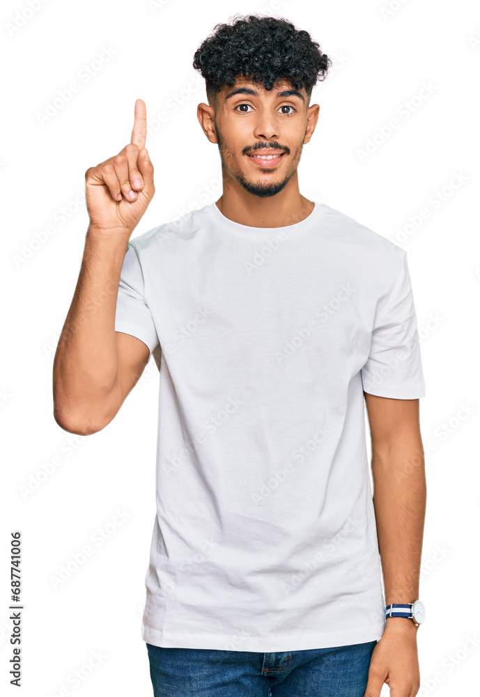 Young arab man wearing casual white t shirt pointing finger up with successful idea. exited and happy. number one. Young arab man wearing casual white t shirt pointing finger up with successful idea. exited and happy. number one.