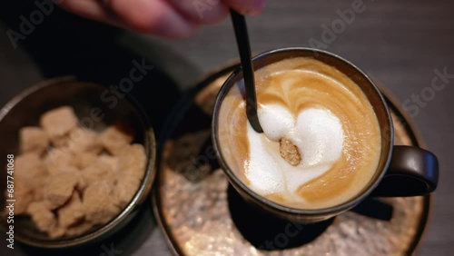 Woman stirring brown sugar into a cappuccino cup of coffee with white heart photo