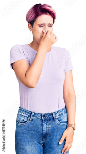 Young beautiful woman with pink hair wearing casual clothes smelling something stinky and disgusting, intolerable smell, holding breath with fingers on nose. bad smell