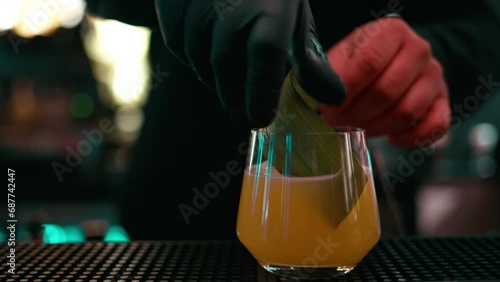 Bartender pouring whiskey cocktail into a glass with big cube of ice from a shaker mixer, adding green leaf photo