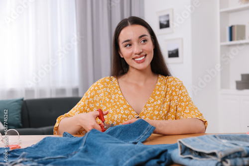 Obraz na plátně Happy woman cutting hem of jeans at table indoors