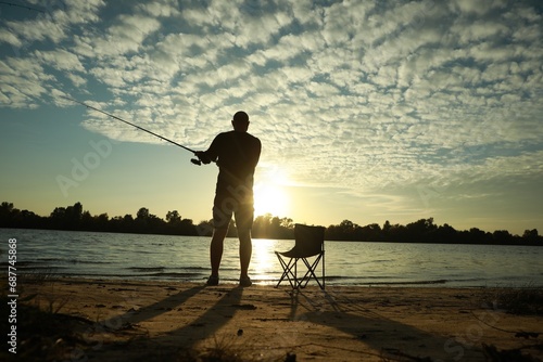 Fisherman with rod fishing at riverside at sunset, back view. Space for text