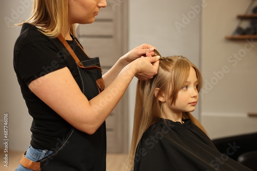 Professional hairdresser braiding girl's hair in beauty salon