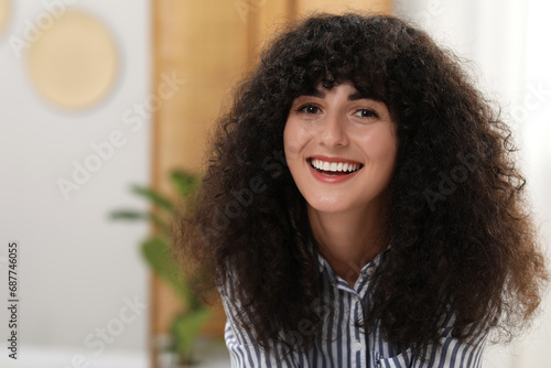 Portrait of beautiful woman with curly hair indoors. Attractive lady smiling and looking into camera. Space for text