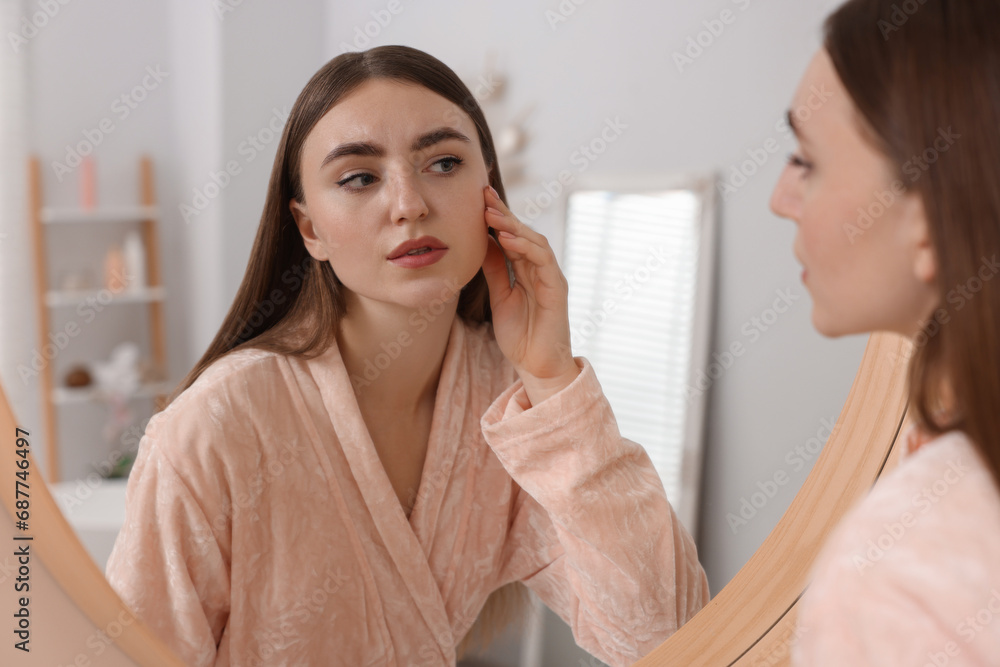 Young woman with skin problem looking at mirror indoors Young woman with skin problem looking at mirror indoors