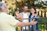 Friendly relationship with neighbours. Happy couple greeting senior man near fence outdoors