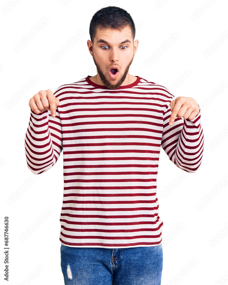 Young handsome man wearing striped sweater pointing down with fingers showing advertisement, surprised face and open mouth Young handsome man wearing striped sweater pointing down with fingers showing advertisement, surprised face and open mouth