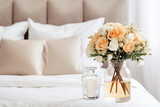 In a modern bedroom with Scandinavian interior design, a glass vase with a flower bouquet sits near a bed adorned with white and beige bedding.

