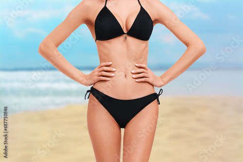 Woman in stylish black bikini on sandy beach near sea, closeup