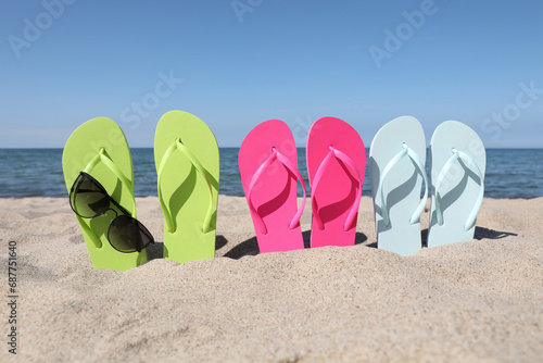Stylish colorful flip flops and sunglasses on beach sand