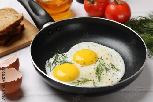 Frying pan with tasty cooked eggs, dill and other products on white tiled table, closeup