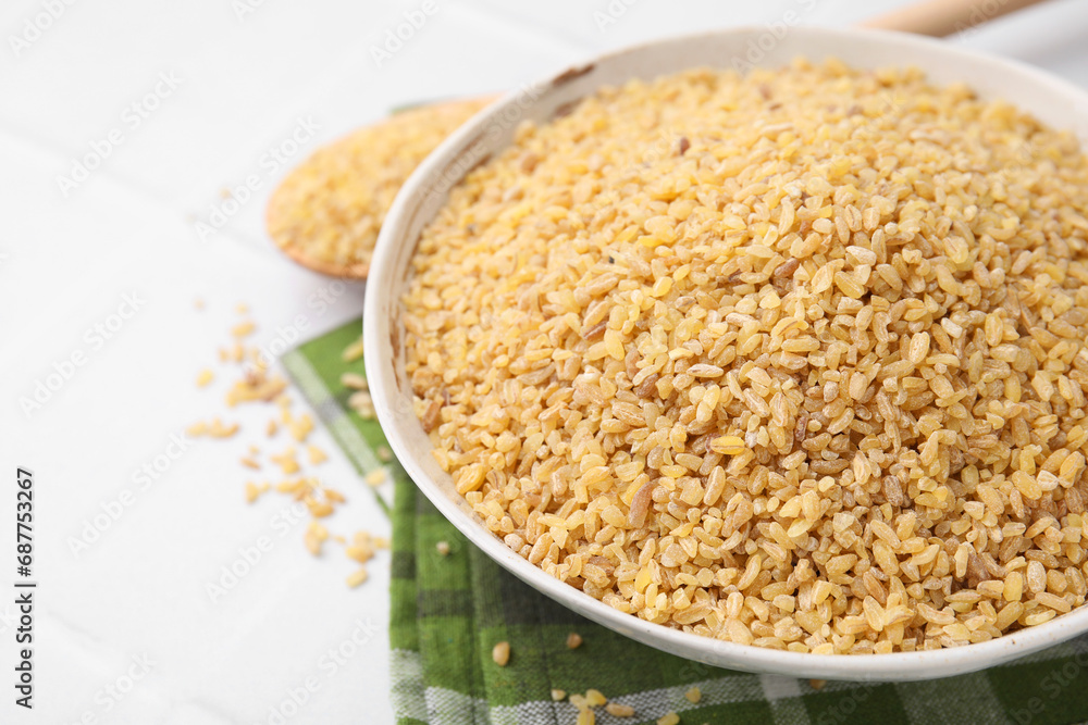 Raw bulgur in bowl on white table, closeup Raw bulgur in bowl on white table, closeup