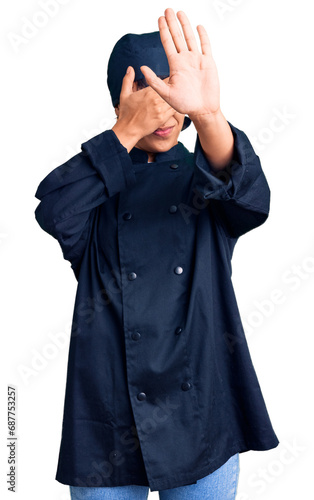 Young brunette woman with short hair wearing professional cook uniform covering eyes with hands and doing stop gesture with sad and fear expression. embarrassed and negative concept.