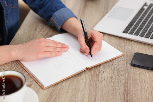 Young woman writing in notebook at wooden table, closeup
