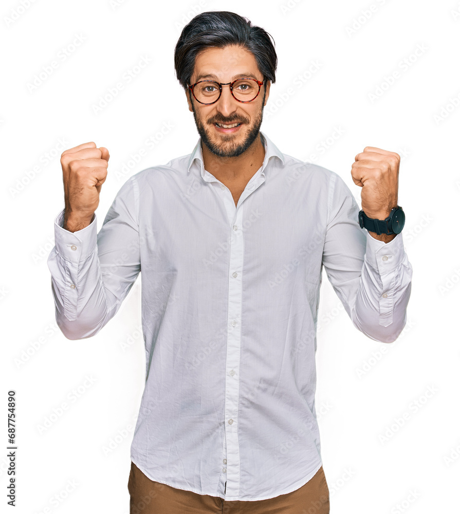 Young hispanic man wearing business shirt and glasses celebrating surprised and amazed for success with arms raised and open eyes. winner concept. Young hispanic man wearing business shirt and glasses celebrating surprised and amazed for success with arms raised and open eyes. winner concept.