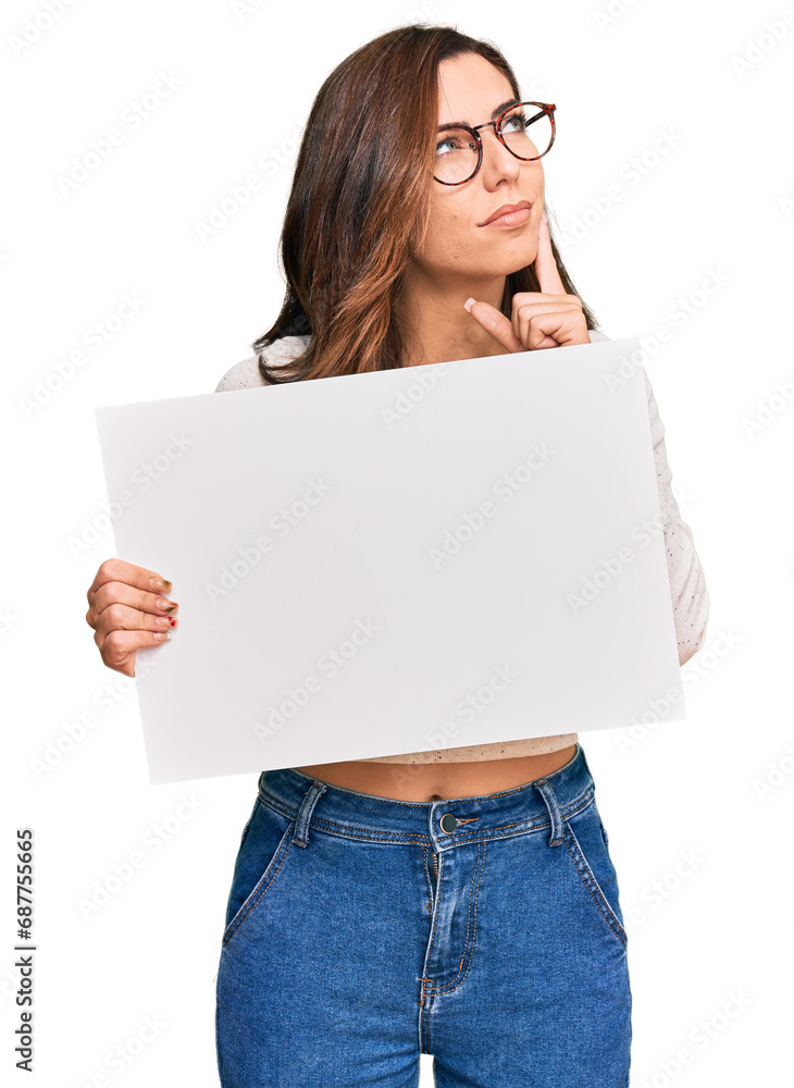 Young brunette woman holding blank empty banner serious face thinking about question with hand on chin, thoughtful about confusing idea Young brunette woman holding blank empty banner serious face thinking about question with hand on chin, thoughtful about confusing idea