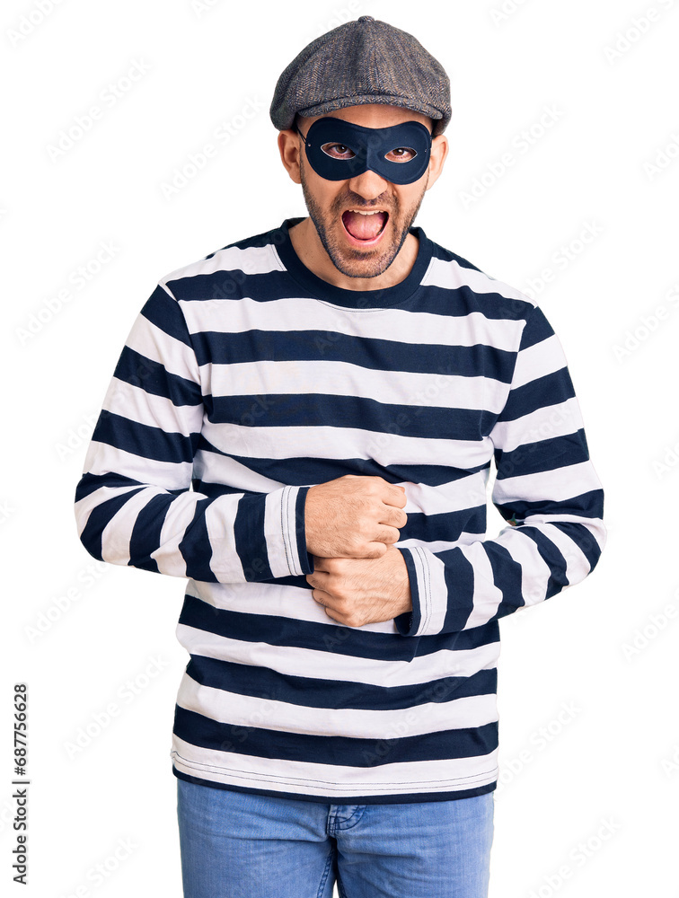 Young handsome man wearing burglar mask smiling and laughing hard out loud because funny crazy joke with hands on body. Young handsome man wearing burglar mask smiling and laughing hard out loud because funny crazy joke with hands on body.